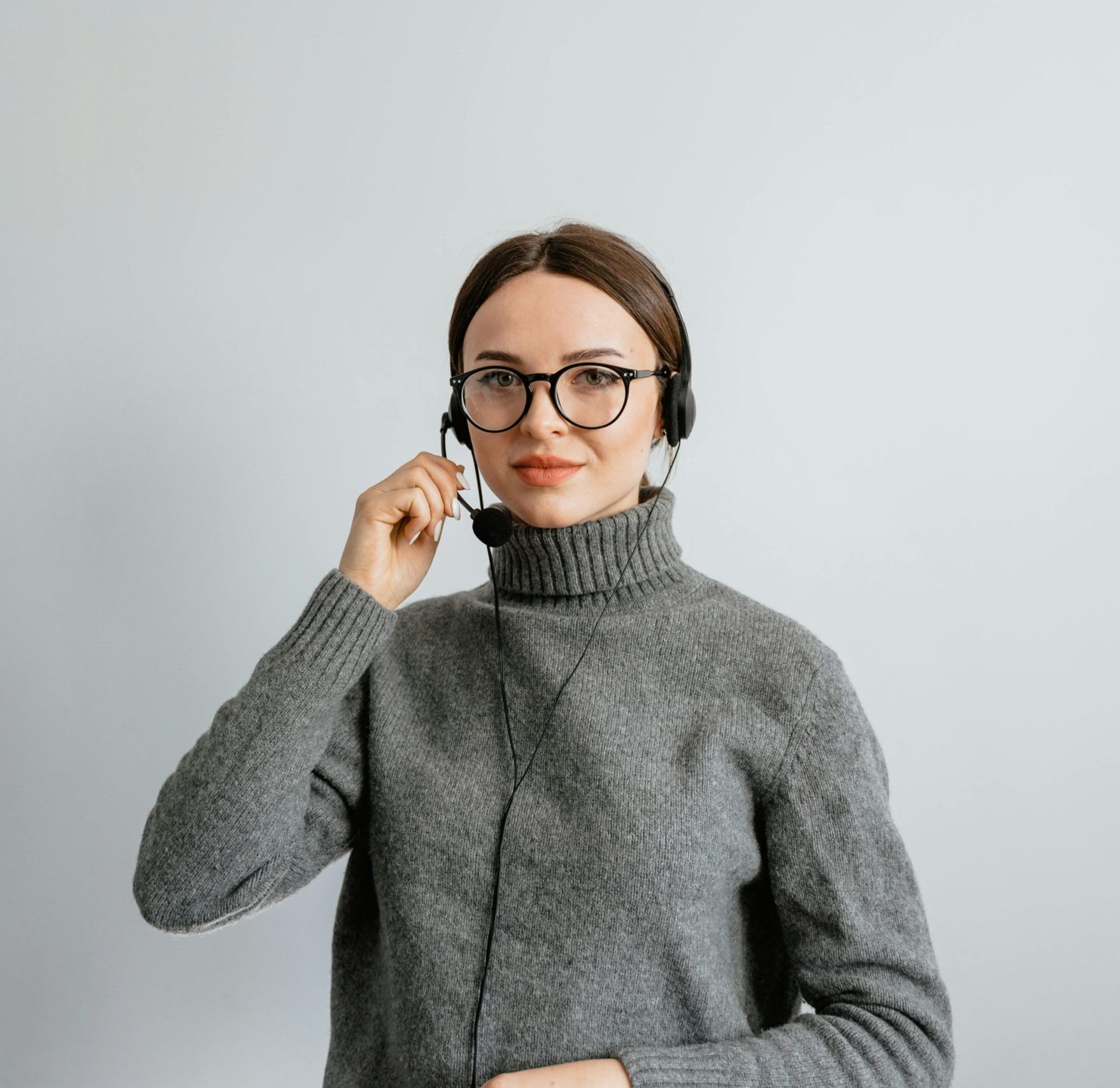 Caucasian woman in gray sweater and glasses providing customer support using a headset in an office.